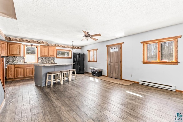 kitchen featuring black fridge with ice dispenser, wood-type flooring, a kitchen island, baseboard heating, and a kitchen bar