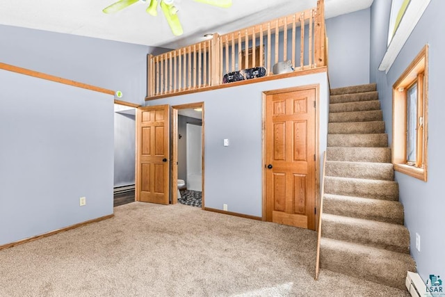 interior space featuring carpet, a towering ceiling, a baseboard heating unit, ceiling fan, and baseboards