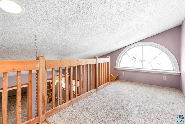 hall with carpet floors, vaulted ceiling, and a textured ceiling