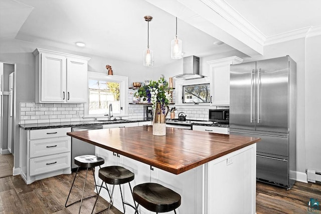 kitchen featuring butcher block countertops, appliances with stainless steel finishes, dark wood-style flooring, wall chimney range hood, and a sink