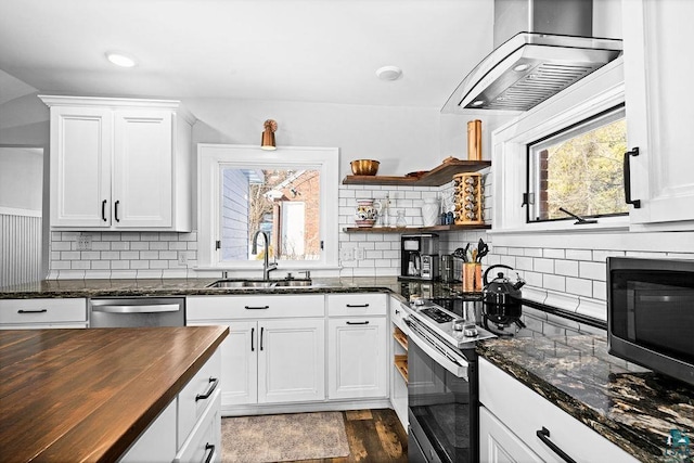 kitchen with stainless steel appliances, butcher block countertops, a sink, white cabinetry, and wall chimney exhaust hood