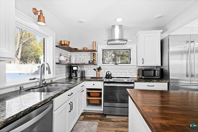 kitchen featuring backsplash, appliances with stainless steel finishes, a sink, wall chimney range hood, and dark stone countertops