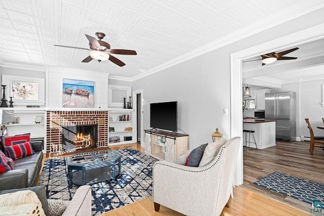 living area with a fireplace, ornamental molding, ceiling fan, wood finished floors, and baseboards