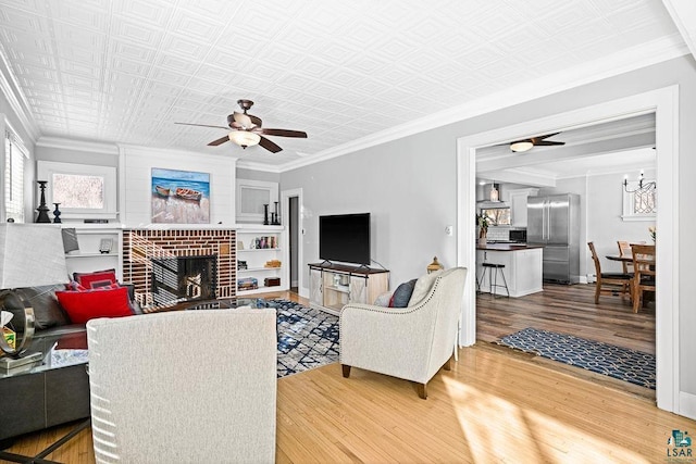 living area featuring an ornate ceiling, ceiling fan, wood finished floors, crown molding, and a fireplace