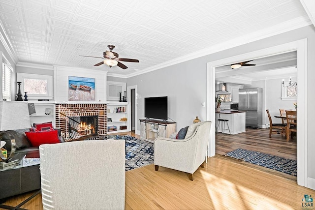 living area featuring ceiling fan, a fireplace, wood finished floors, and crown molding