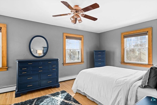 bedroom featuring a baseboard heating unit, baseboard heating, light wood-style flooring, and baseboards