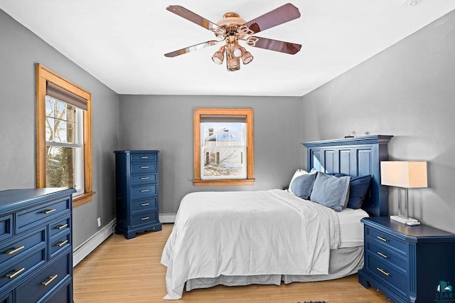 bedroom with baseboard heating, light wood-type flooring, a ceiling fan, and baseboards