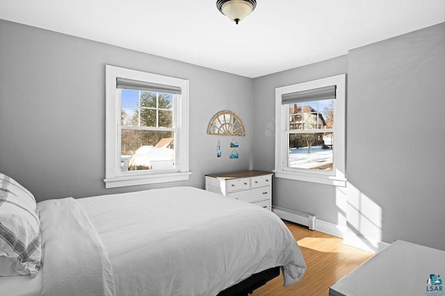 bedroom featuring light wood-style flooring, multiple windows, baseboards, and baseboard heating