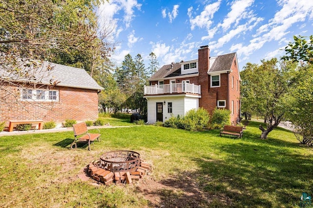 back of house featuring an outdoor fire pit, a balcony, brick siding, a lawn, and a chimney