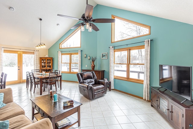 living area with high vaulted ceiling, ceiling fan with notable chandelier, baseboards, and light tile patterned flooring