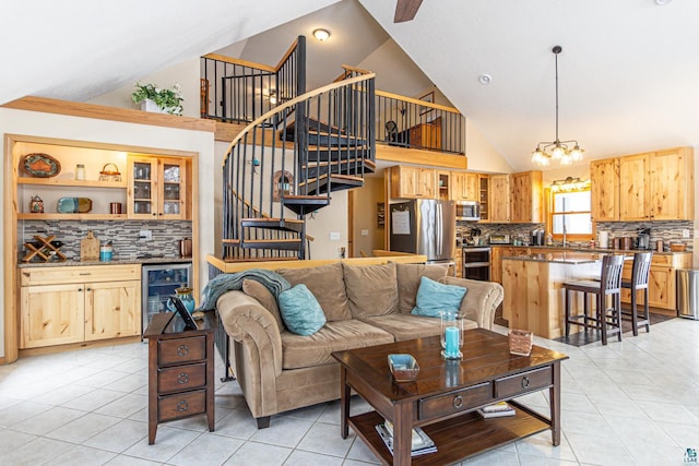 living area featuring light tile patterned floors, high vaulted ceiling, wine cooler, a chandelier, and stairs