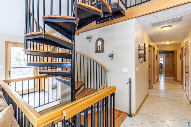 stairway featuring baseboards, tile patterned flooring, visible vents, and a textured ceiling