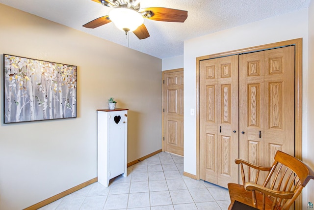 living area featuring light tile patterned floors, ceiling fan, a textured ceiling, and baseboards