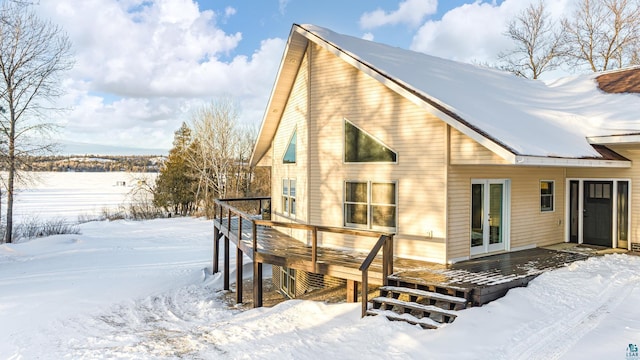 snow covered rear of property with french doors and a wooden deck