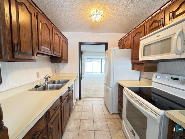 kitchen featuring light tile patterned floors, light countertops, a sink, a textured ceiling, and white appliances