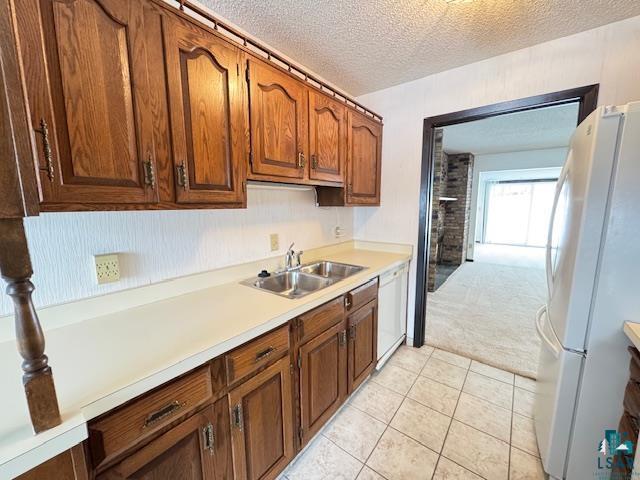 kitchen with white appliances, light countertops, a textured ceiling, a sink, and light tile patterned flooring