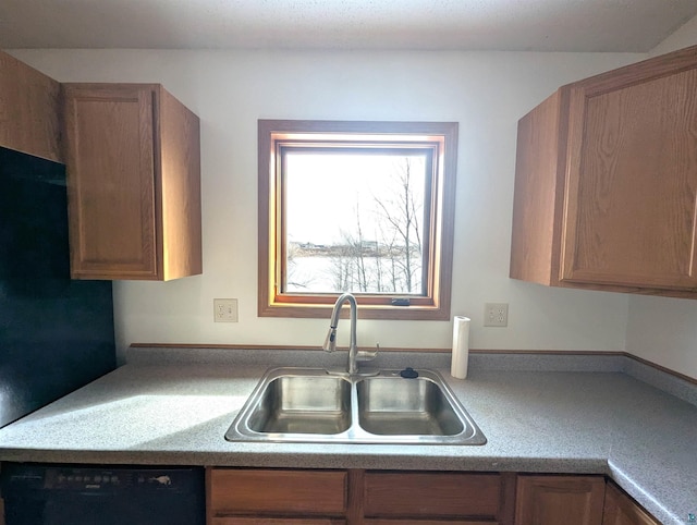 kitchen featuring brown cabinetry, black dishwasher, light countertops, and a sink