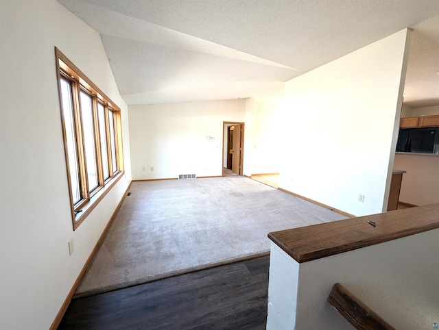 empty room with dark wood-style floors, lofted ceiling, visible vents, dark carpet, and baseboards