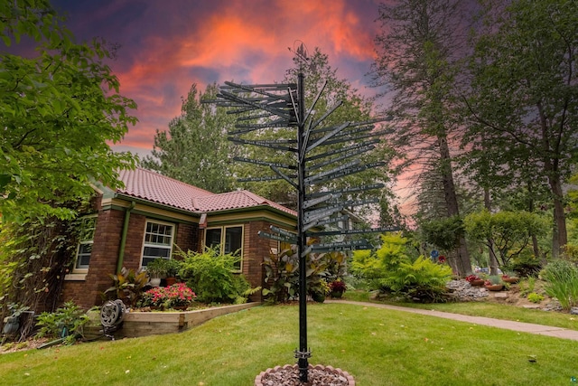 view of front of house with a tile roof, a lawn, and brick siding