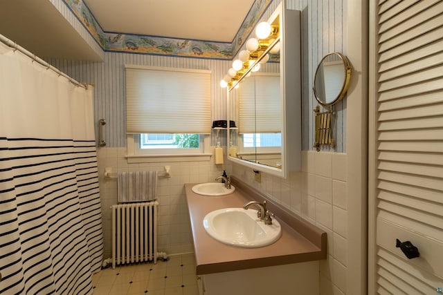 bathroom featuring radiator, wallpapered walls, tile walls, and a sink