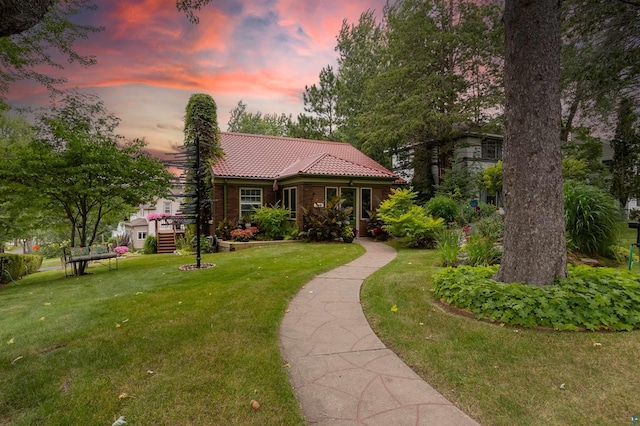 view of front of house featuring a front lawn, a chimney, a tile roof, and brick siding