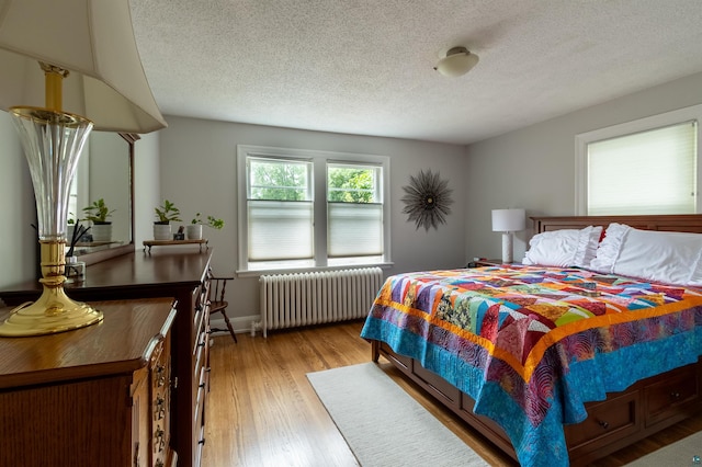 bedroom with radiator, light wood finished floors, baseboards, and a textured ceiling