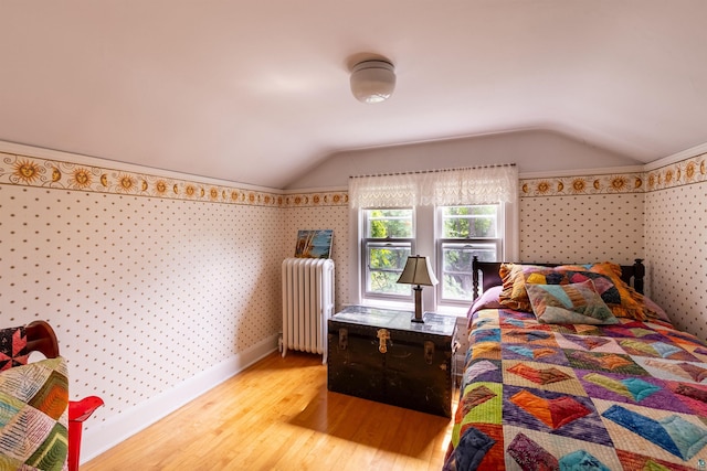 bedroom with lofted ceiling, radiator heating unit, wood finished floors, baseboards, and wallpapered walls