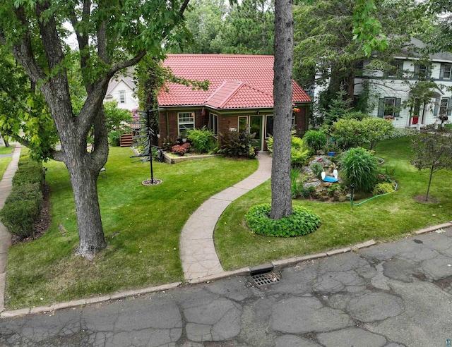 view of front of home featuring a tiled roof, brick siding, and a front yard