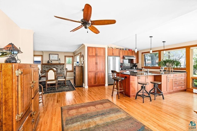 kitchen featuring high end refrigerator, hanging light fixtures, light wood-style floors, under cabinet range hood, and a kitchen breakfast bar