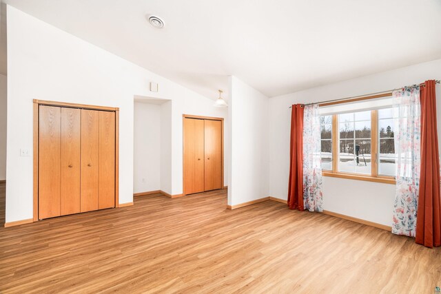 unfurnished bedroom featuring light wood finished floors, baseboards, visible vents, lofted ceiling, and two closets