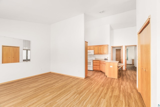 kitchen with white appliances, light wood finished floors, a peninsula, light countertops, and high vaulted ceiling