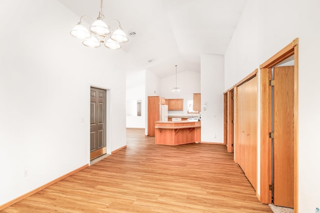 corridor with light wood finished floors, baseboards, high vaulted ceiling, and an inviting chandelier