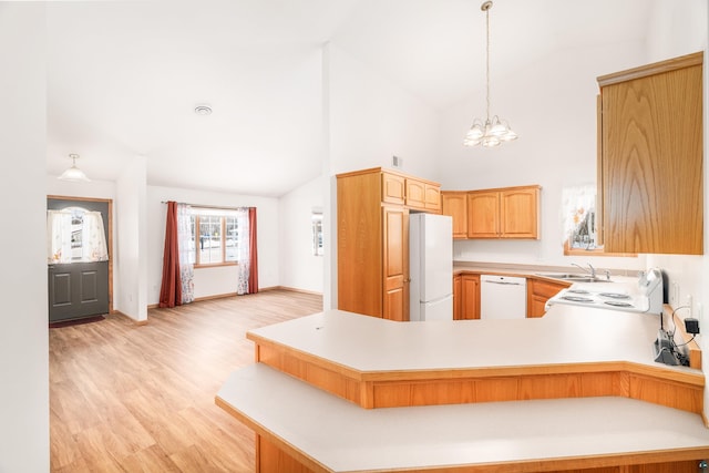 kitchen with a peninsula, white appliances, a sink, light countertops, and light wood-type flooring