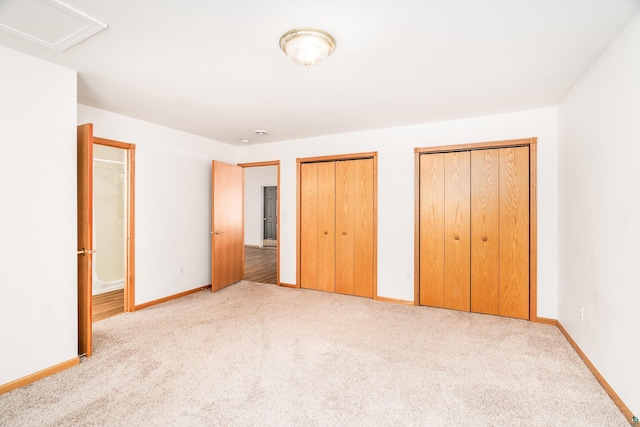 unfurnished bedroom with carpet, two closets, attic access, and baseboards