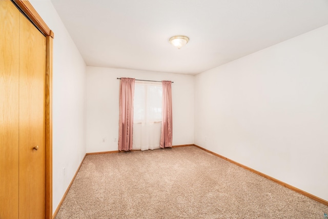 spare room with baseboards and light colored carpet