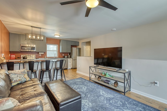 living room with light wood-style floors, baseboards, and a ceiling fan