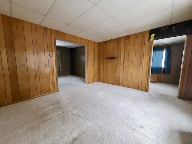 carpeted spare room with a paneled ceiling and wooden walls