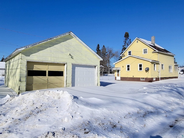 view of snow covered exterior featuring a garage and an outbuilding