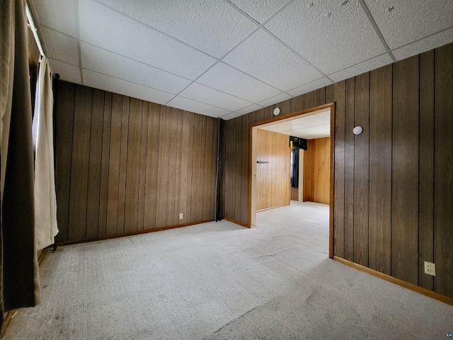 empty room with wooden walls, a drop ceiling, and light colored carpet