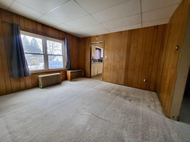 spare room with a paneled ceiling, carpet flooring, wood walls, and radiator heating unit