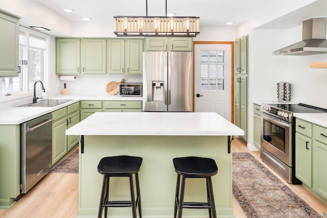 kitchen with appliances with stainless steel finishes, green cabinetry, a sink, and wall chimney exhaust hood