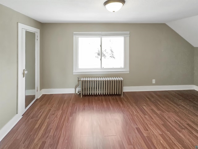 additional living space with vaulted ceiling, radiator, wood finished floors, and baseboards