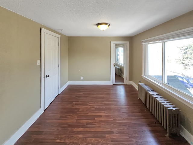 unfurnished room featuring dark wood-style floors, radiator, a textured ceiling, and baseboards