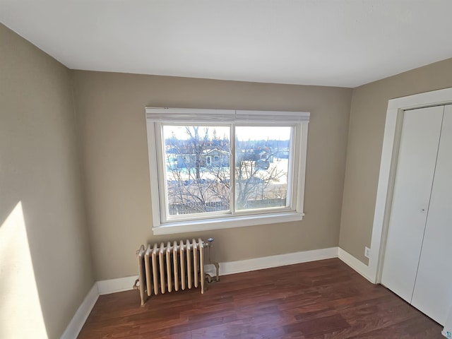 unfurnished bedroom featuring dark wood finished floors, a closet, radiator heating unit, and baseboards