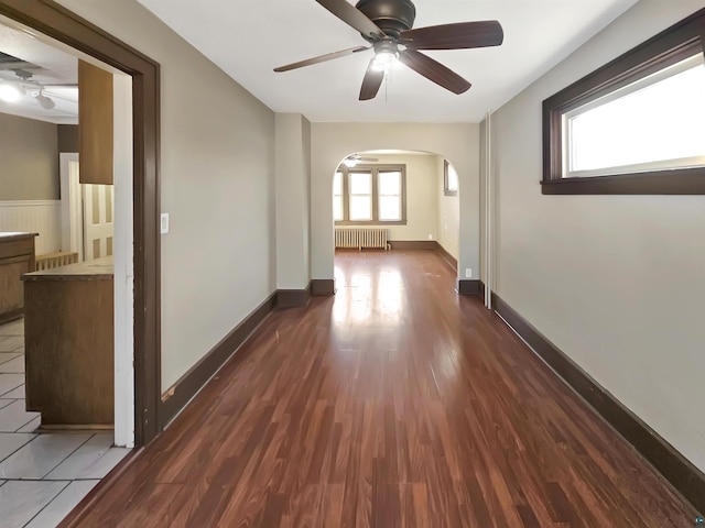 empty room featuring radiator, baseboards, ceiling fan, arched walkways, and dark wood-style flooring