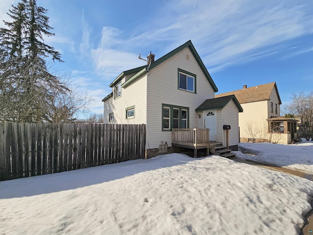 snow covered back of property featuring fence, a chimney, and a wooden deck