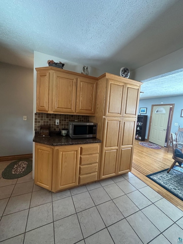 kitchen with light tile patterned floors, stainless steel microwave, backsplash, and a textured ceiling