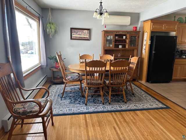 dining space featuring a wall unit AC, an inviting chandelier, light wood-style flooring, a textured ceiling, and baseboard heating