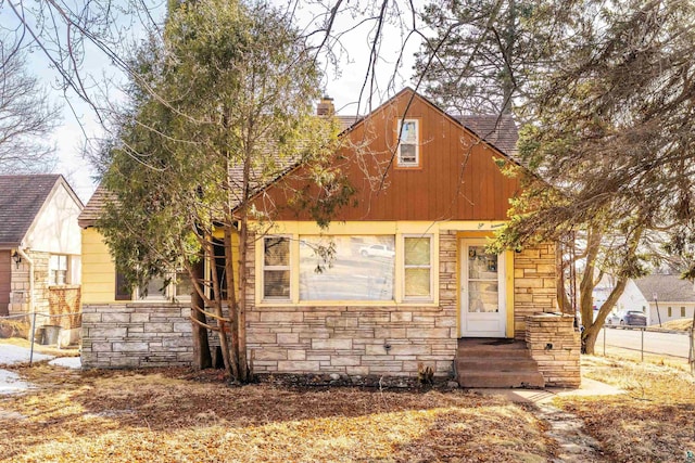 view of front of property with stone siding, entry steps, a chimney, and a shingled roof