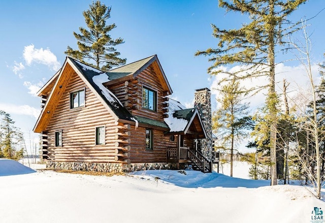 snow covered property with log siding and a chimney